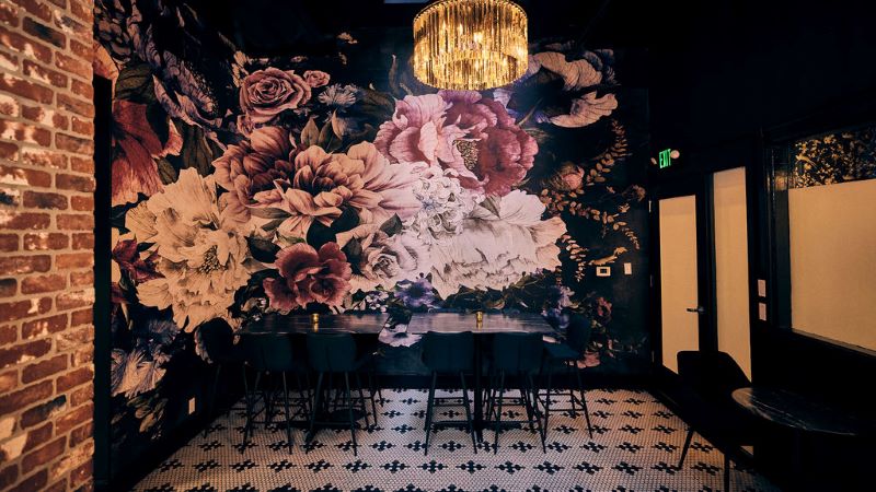 Two black restaurant tables against a large floral mural at the Harlequin.