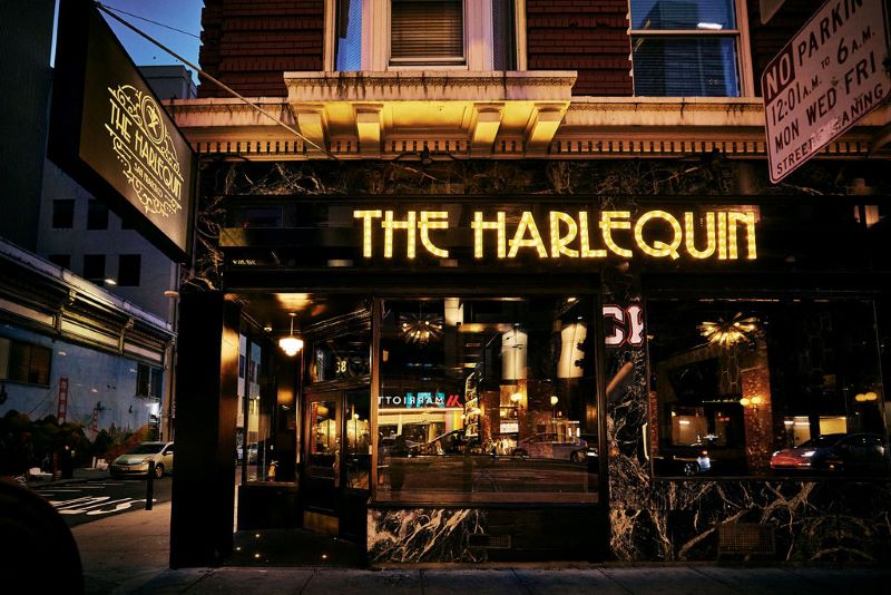 Exterior of The Harlequin with restaurant sign in gold Art Deco luminous lettering. 