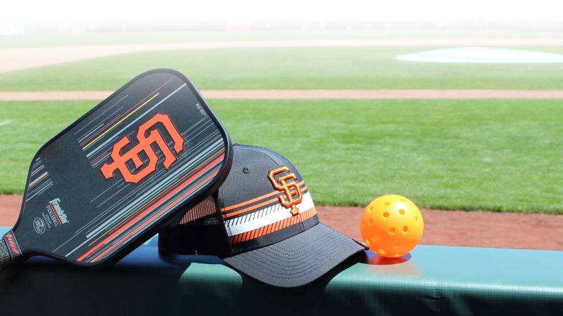An SF Giants-branded pickleball paddle, hat, and whiffle ball.