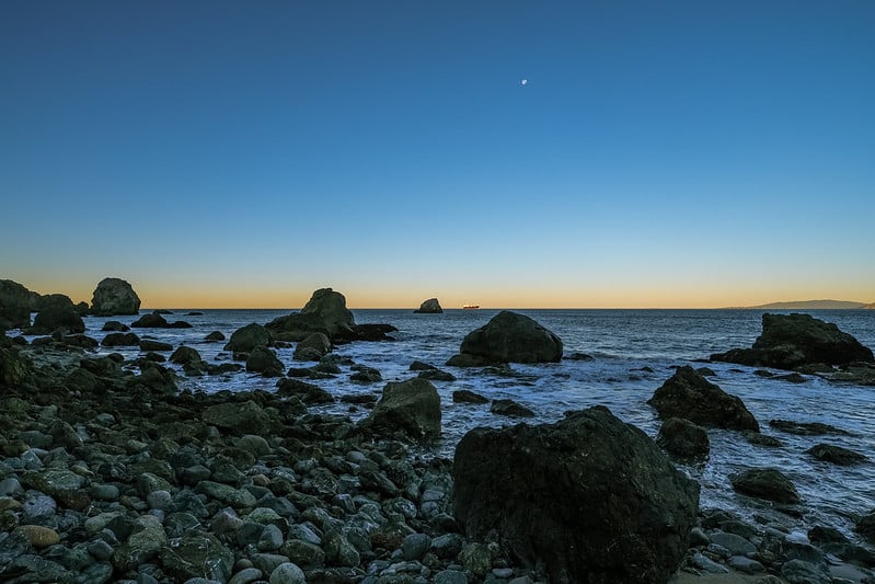 Rocky beach at sunset with large boulders in the waves.