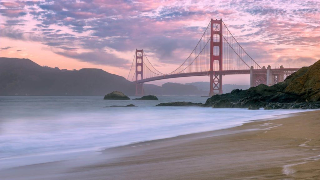 A beach at sunset with Golden Gate Bridge in the distance.