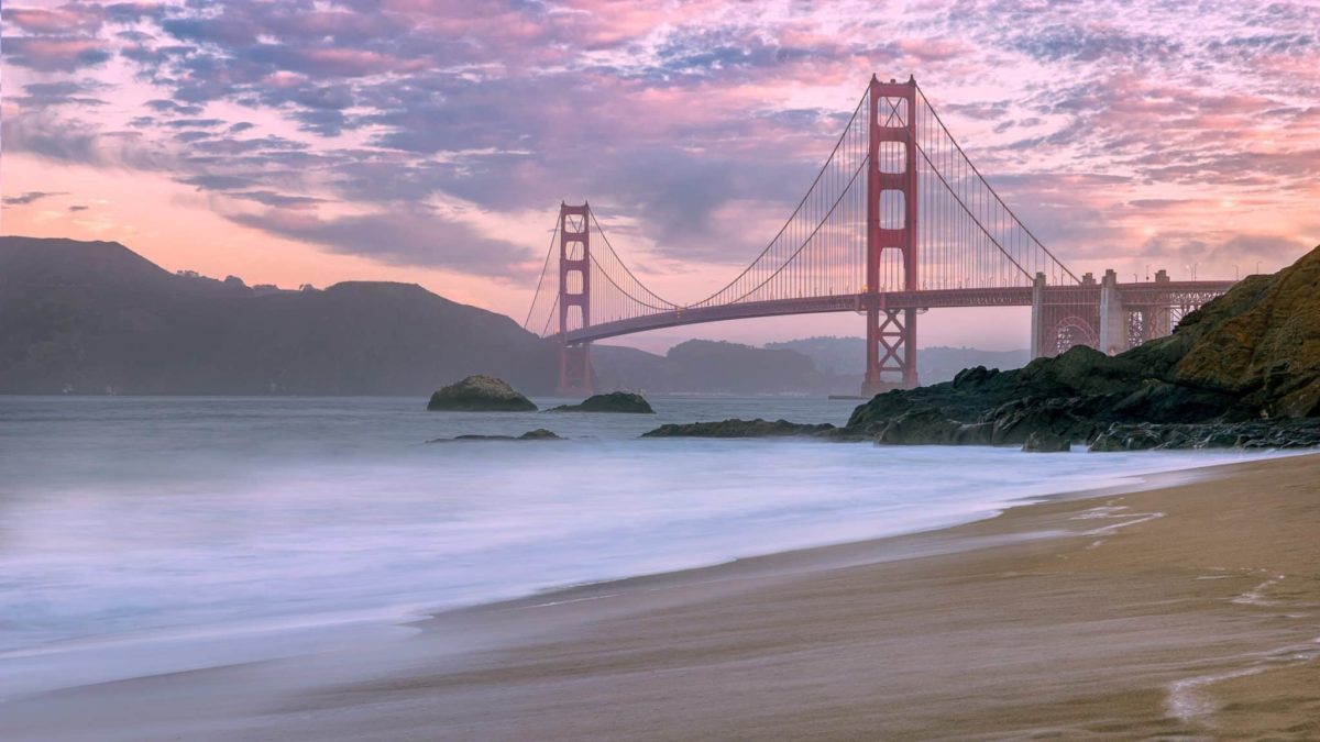 A beach at sunset with Golden Gate Bridge in the distance.