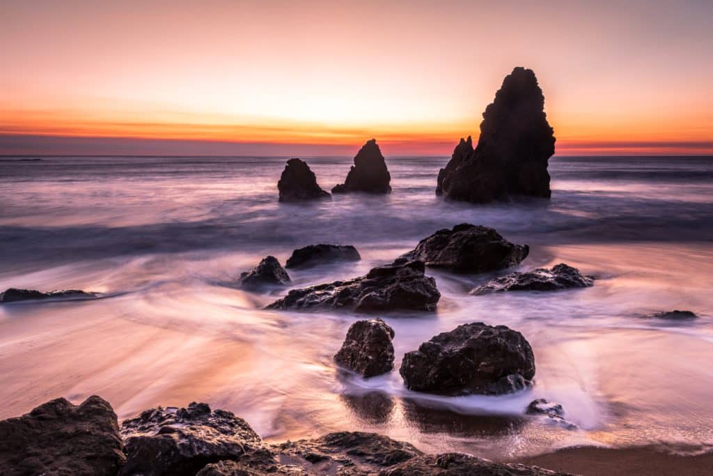 Beach at sunset with waves flowing through rocks.