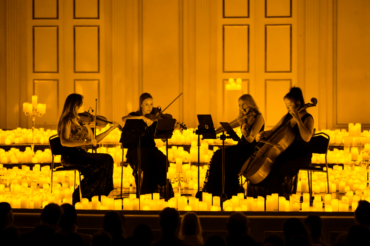 A string quartet performing on a stage surrounded by flickering candles.