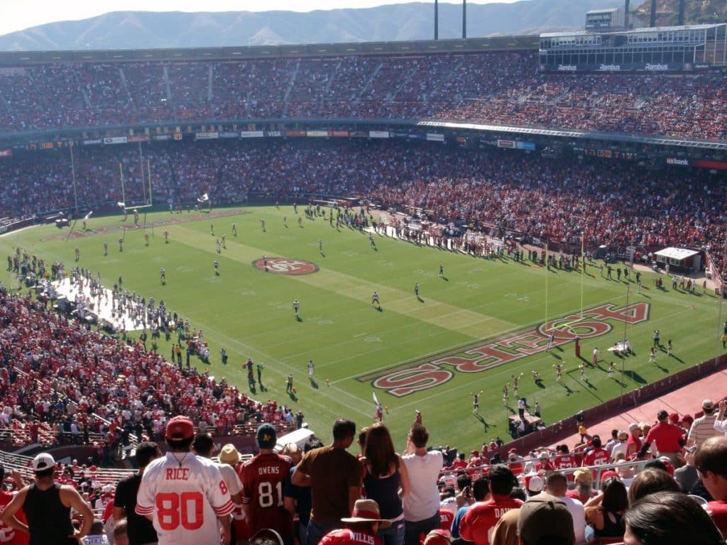 Thousands of fans dressed in red watch a football game at Candlestick Park.