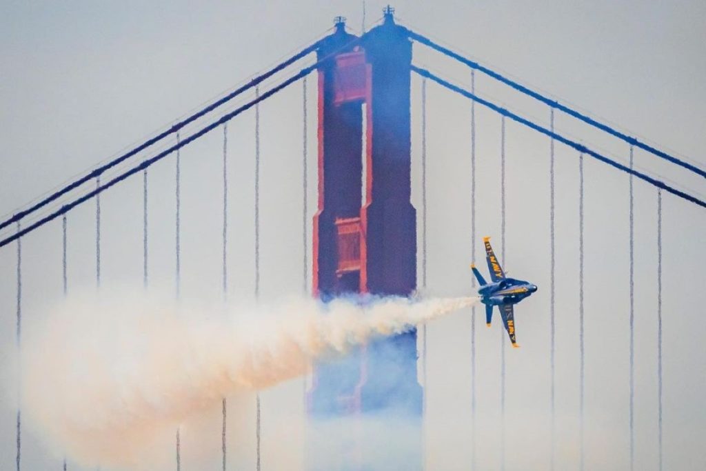 A blue and yellow plane performs a stunt in front of the Golden Gate Bridge.